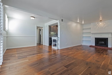 Unfurnished living room with built in shelves, a fireplace with raised hearth, and hardwood / wood-style floors