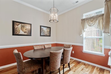 Dining area with wood finished floors, crown molding, and a chandelier