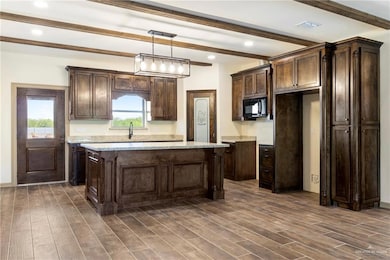 Kitchen featuring dark brown cabinetry, a kitchen island, black microwave, and wood finish floors