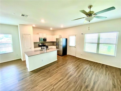 Kitchen featuring stainless steel appliances, white cabinets, dark wood-type flooring, a center island with sink, and recessed lighting