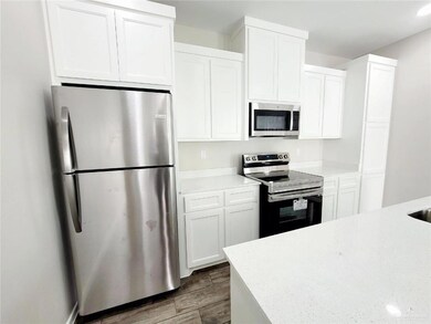 Kitchen featuring appliances with stainless steel finishes, wood finished floors, white cabinetry, and light stone counters