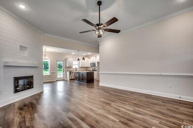 Unfurnished living room with dark wood-style flooring, a large fireplace, crown molding, baseboards, and ceiling fan with notable chandelier