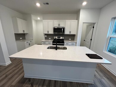Kitchen with stainless steel appliances, white cabinets, an island with sink, dark wood-style flooring, and decorative backsplash