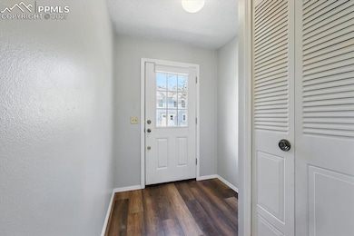 Doorway with baseboards, dark wood-type flooring, and a textured ceiling