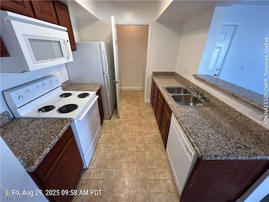 Kitchen with white appliances, dark stone counters, a peninsula, and dark brown cabinetry
