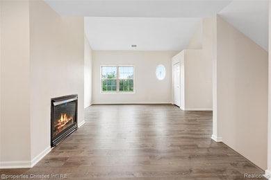 Unfurnished living room featuring wood finished floors, a glass covered fireplace, and vaulted ceiling