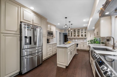 Kitchen featuring appliances with stainless steel finishes, ventilation hood, dark wood-style floors, light stone countertops, and glass insert cabinets