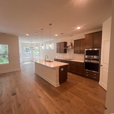 Kitchen with decorative backsplash, hanging light fixtures, dark brown cabinets, stainless steel appliances, and an island with sink
