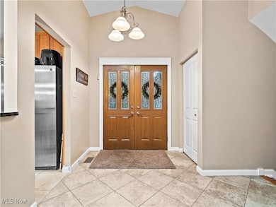 Foyer entrance with vaulted ceiling, a chandelier, and light tile patterned floors