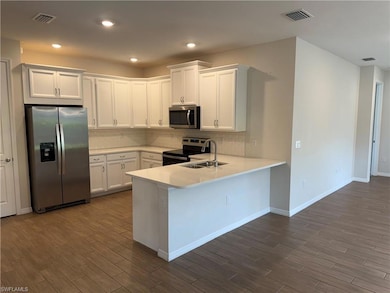 Kitchen with stainless steel appliances, dark wood-style flooring, backsplash, white cabinetry, and recessed lighting