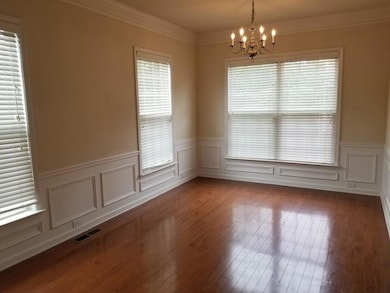 Unfurnished room featuring ornamental molding, a chandelier, wood finished floors, wainscoting, and a decorative wall