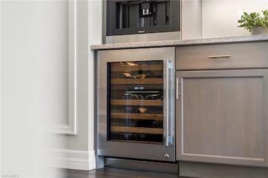 Bar with wine cooler, baseboards, a textured wall, and wood finished floors