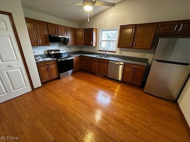 Kitchen with appliances with stainless steel finishes, vaulted ceiling, light wood-style floors, ceiling fan, and brown cabinetry