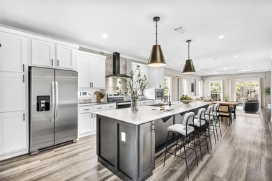 Kitchen with stainless steel appliances, white cabinets, a breakfast bar area, a large island, and wall chimney exhaust hood