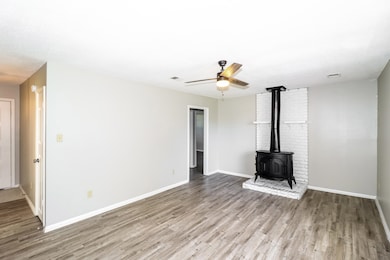 Unfurnished living room with a wood stove, wood finished floors, ceiling fan, and baseboards