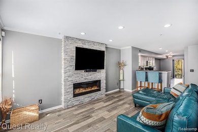 Living room with crown molding, wood finished floors, recessed lighting, and a stone fireplace