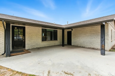 Doorway to property with roof with shingles, brick siding, and a patio area