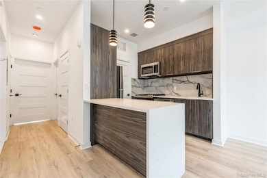 Kitchen featuring dark brown cabinets, light stone countertops, decorative backsplash, modern cabinets, and pendant lighting. The pictures represent the model unit.