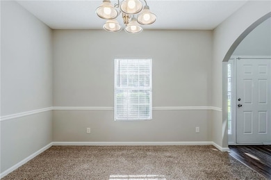 Carpeted foyer entrance with arched walkways, a chandelier, and baseboards