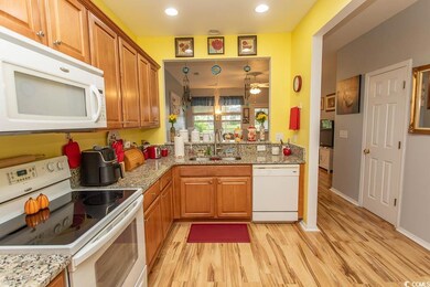 Kitchen featuring white appliances, light stone countertops, light wood finished floors, brown cabinets, and recessed lighting