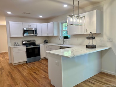 Kitchen featuring appliances with stainless steel finishes, a peninsula, hanging light fixtures, light wood-type flooring, and white cabinetry