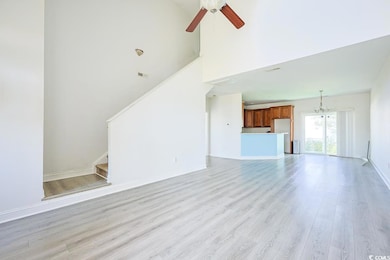 Unfurnished living room with stairway, light wood-style floors, a high ceiling, a chandelier, and ceiling fan