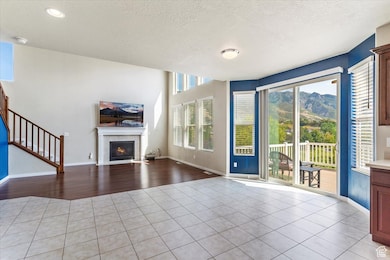 Unfurnished living room featuring a textured ceiling, light tile patterned floors, a tiled fireplace, and stairway