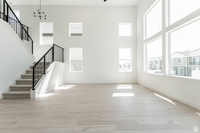 Unfurnished living room featuring stairway, light wood-style flooring, plenty of natural light, a high ceiling, and a chandelier
