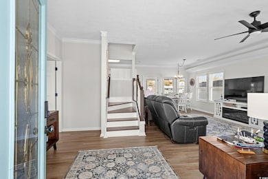 Living room featuring ornamental molding, light wood-style floors, stairs, ceiling fan, and a chandelier