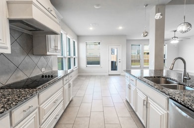 Kitchen featuring dark stone countertops, white cabinetry, premium range hood, dishwasher, and light tile patterned floors