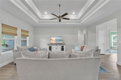 Living room with a ceiling fan, a raised ceiling, ornamental molding, and a healthy amount of sunlight