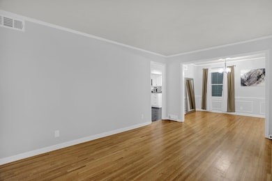Unfurnished living room with ornamental molding, light wood-style floors, and a chandelier