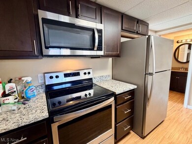 Kitchen with appliances with stainless steel finishes, dark brown cabinets, light wood-style flooring, light stone counters, and a drop ceiling