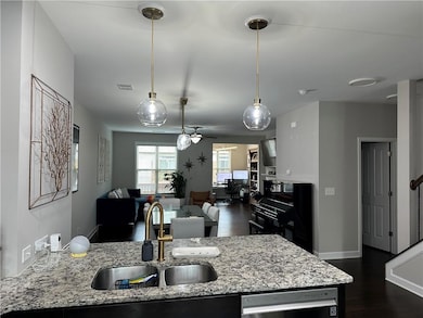 Kitchen featuring light stone counters, open floor plan, dark wood-style floors, pendant lighting, and dishwasher