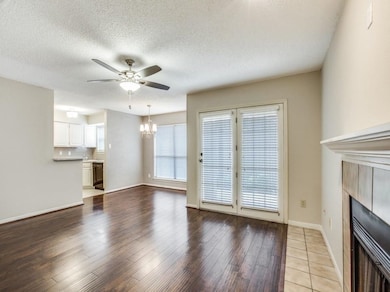 Unfurnished living room with ceiling fan with notable chandelier, light wood-type flooring, a tile fireplace, and a textured ceiling