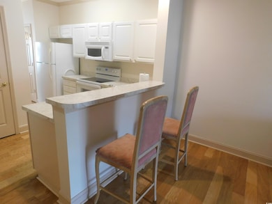 Kitchen featuring white appliances, a kitchen bar, light wood-style floors, a peninsula, and light countertops