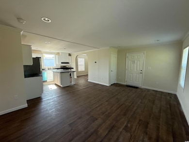 Unfurnished living room with arched walkways, ornamental molding, dark wood-style flooring, baseboards, and recessed lighting