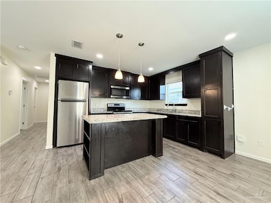 Kitchen with appliances with stainless steel finishes, light wood finished floors, a kitchen island, baseboards, and pendant lighting