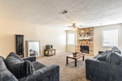 Carpeted living room with a ceiling fan, a textured ceiling, a fireplace, and baseboards