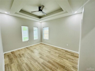 Spare room featuring light wood finished floors, ceiling fan, baseboards, and a raised ceiling