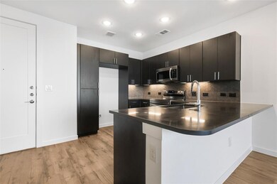 Kitchen with tasteful backsplash, dark countertops, stainless steel appliances, a peninsula, and light wood-style floors