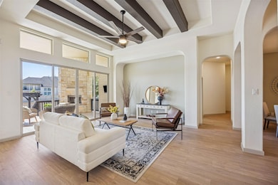 Living area featuring beamed ceiling, ceiling fan, arched walkways, light wood-style flooring, and a stone fireplace
