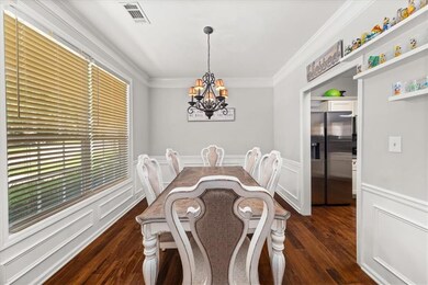 Dining room featuring a chandelier, dark wood-type flooring, ornamental molding, and wainscoting