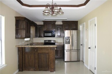 Kitchen featuring dark brown cabinets, appliances with stainless steel finishes, a raised ceiling, and dark stone counters