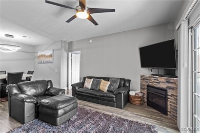 Living room featuring a fireplace, ceiling fan with notable chandelier, a textured ceiling, and wood finished floors