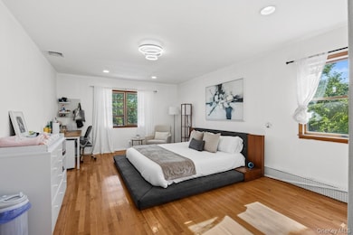 Bedroom featuring hardwood / wood-style floors, a baseboard radiator, an office area, and recessed lighting