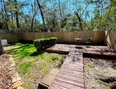 This backyard features a fenced area with a wooden deck, perfect for outdoor seating. The space includes a small grassy area, shrubs, and a surrounding natural wooded backdrop for privacy and tranquility.