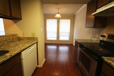 Kitchen with stainless steel range with electric stovetop, under cabinet range hood, light stone countertops, white dishwasher, and crown molding