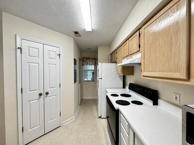 Kitchen featuring electric stove, under cabinet range hood, light countertops, freestanding refrigerator, and a textured ceiling
