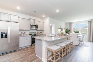 Kitchen with sink, light stone counters, appliances with stainless steel finishes, an island with sink, and light hardwood / wood-style floors